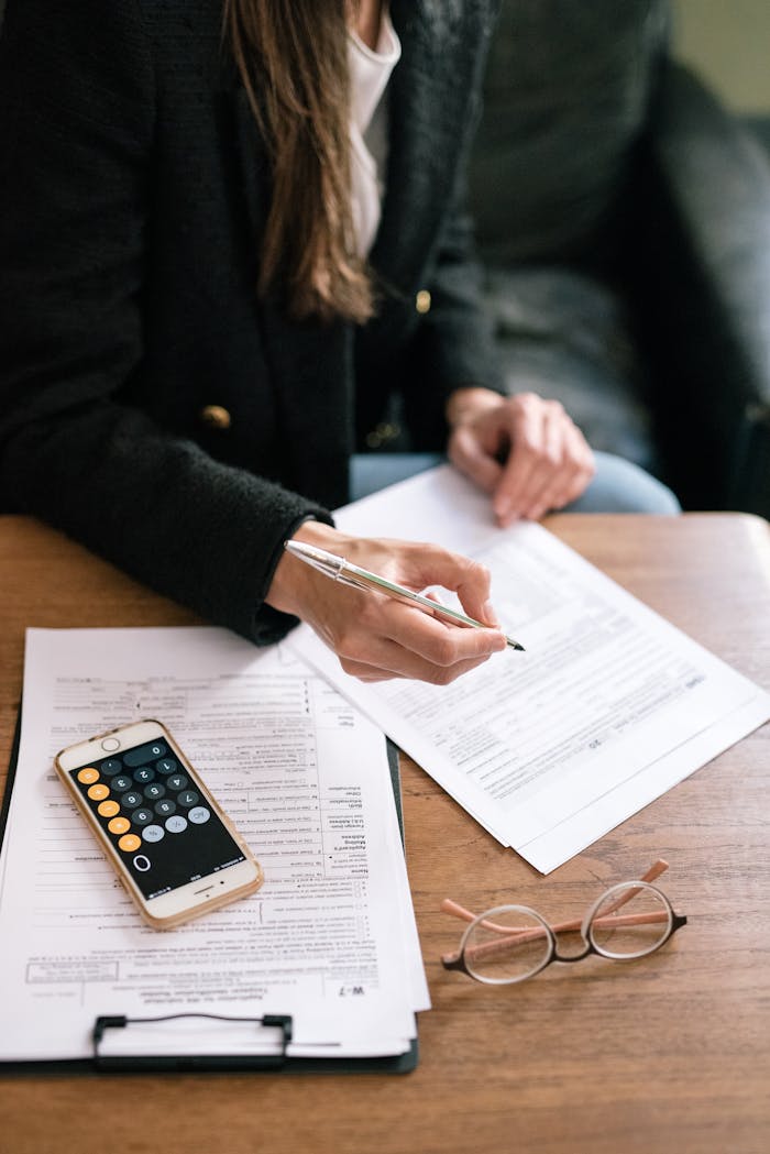 A woman reviewing financial documents with a calculator and glasses on a table.